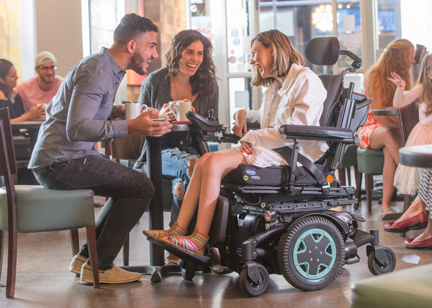 A woman using a TDX SP2 power chair laughs in a cafe with her friends